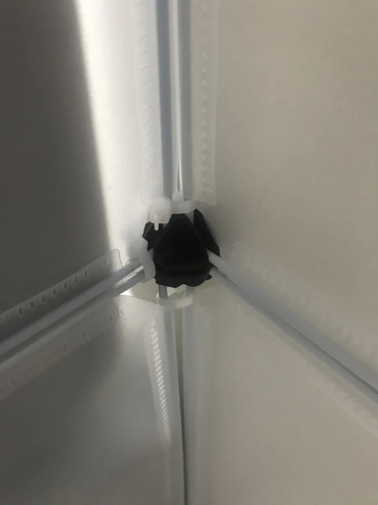 Round black plastic connector joining opaque enclosure panels, reinforced with a cable tie
