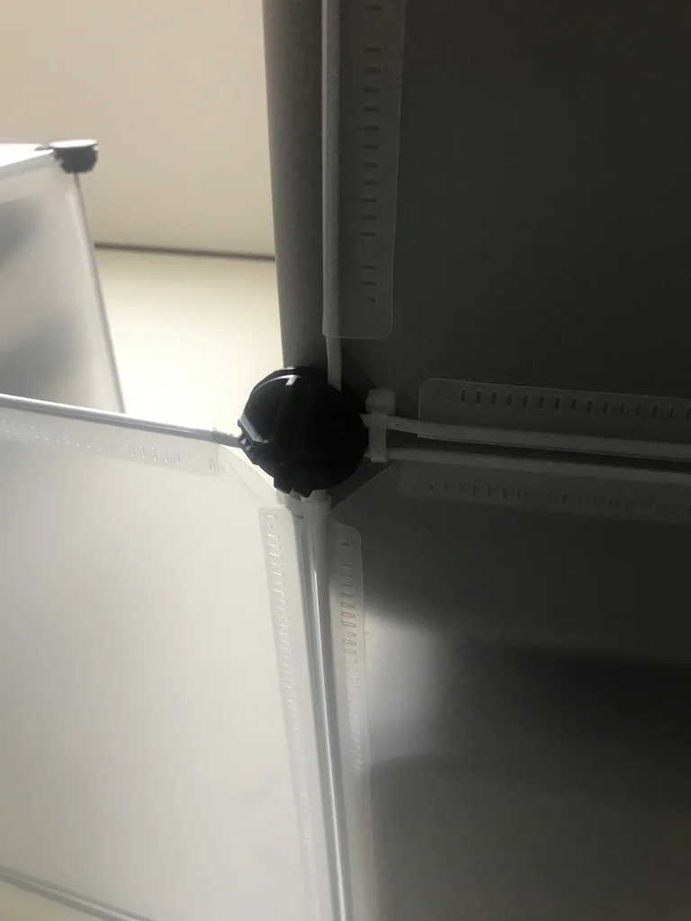 Close-up of an enclosure panel joint locked with a round connector and cinched cable ties