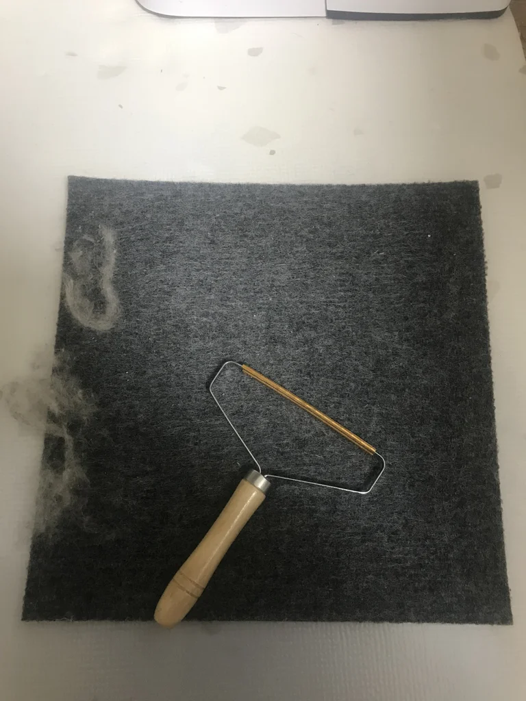 Carpet tile from the enclosure platform covered in rabbit fur, with a manual lint scraper