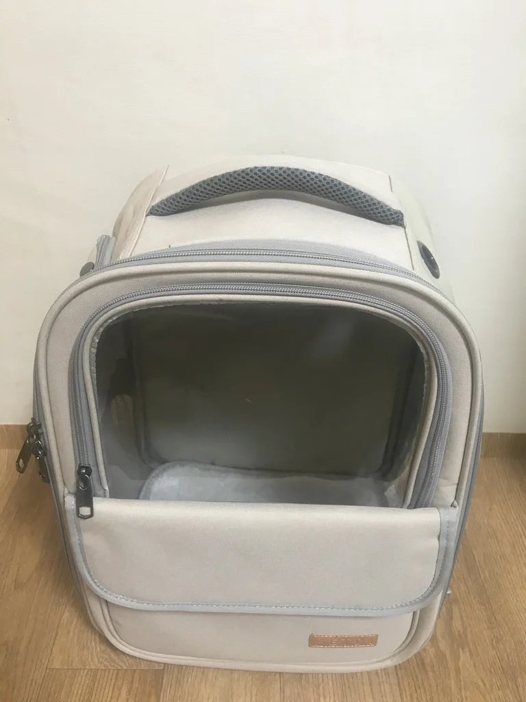 Backpack-style rabbit carrier with transparent front panel, standing on wooden floor